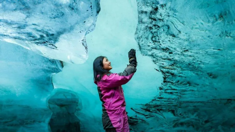Visitor in a pink snowsuit touching the turquoise wall of a natural ice cave on a Langjökull snowmobile and ice cave day tour from Reykjavík, Iceland