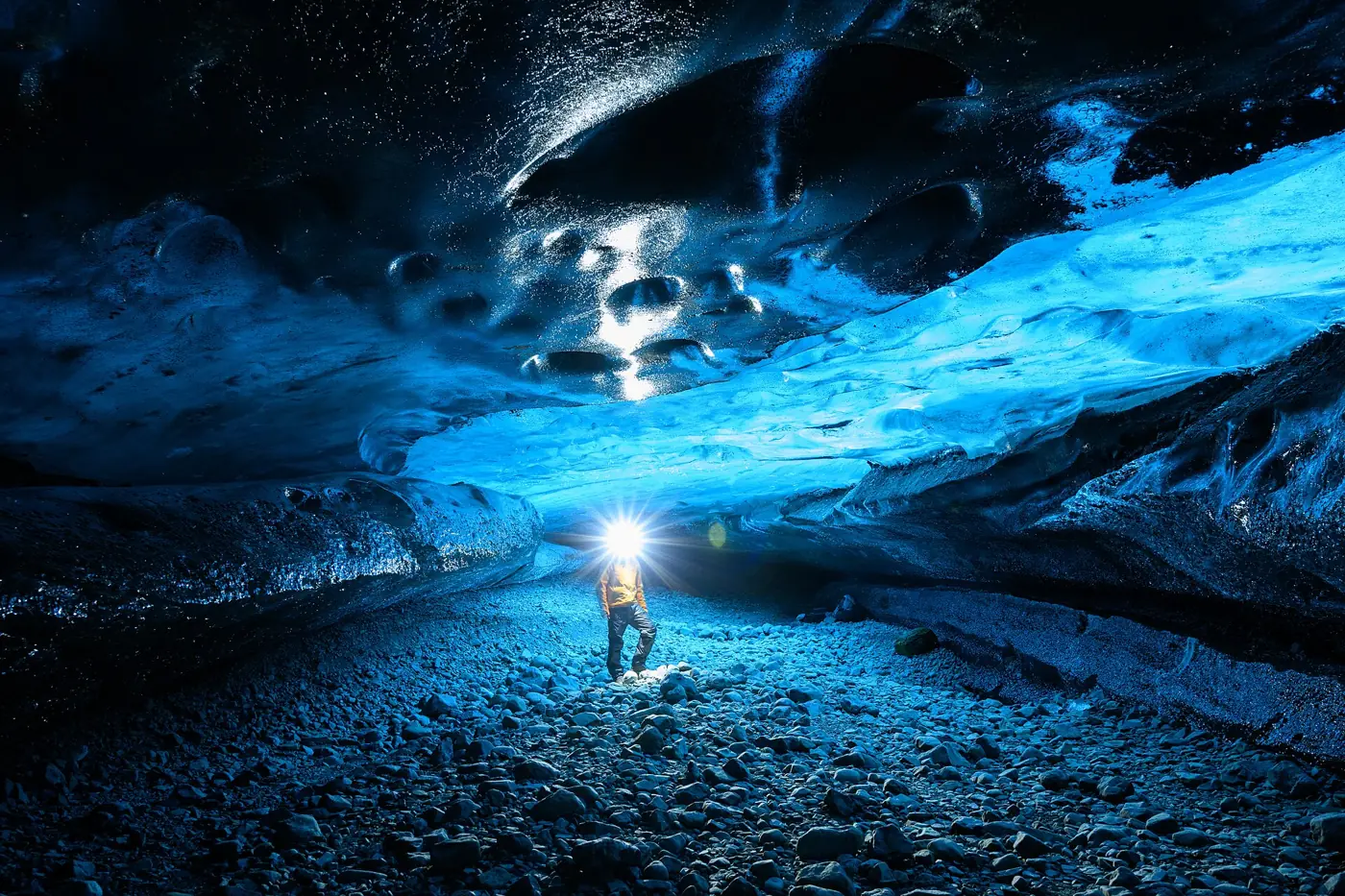 A visitor with a headlamp standing in a blue ice cave under Vatnajökull, the kind of chamber an Iceland ice cave day tour reaches in December